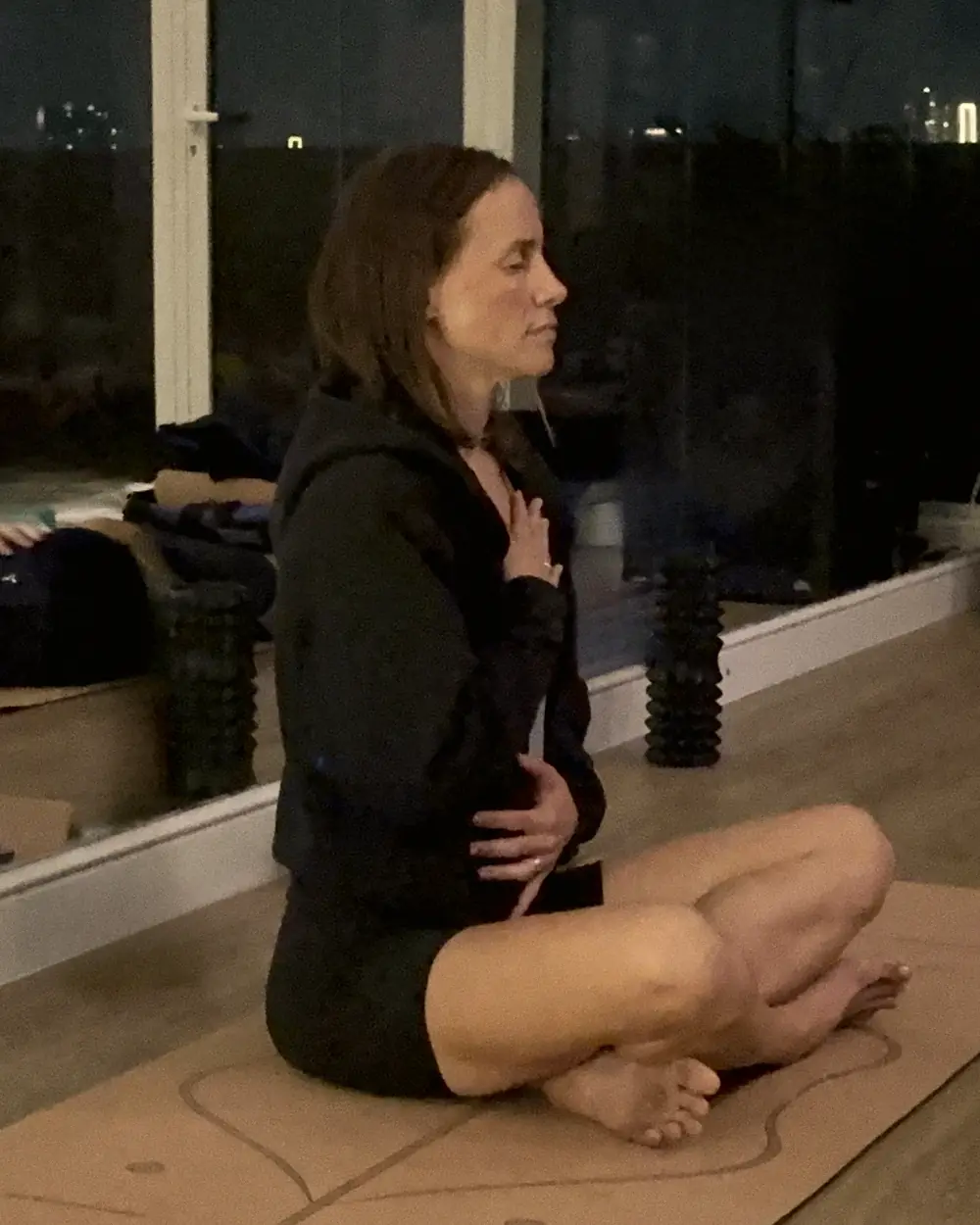 Colette seated cross-legged, eyes closed, one hand on her chest and one on her belly, leading the breath