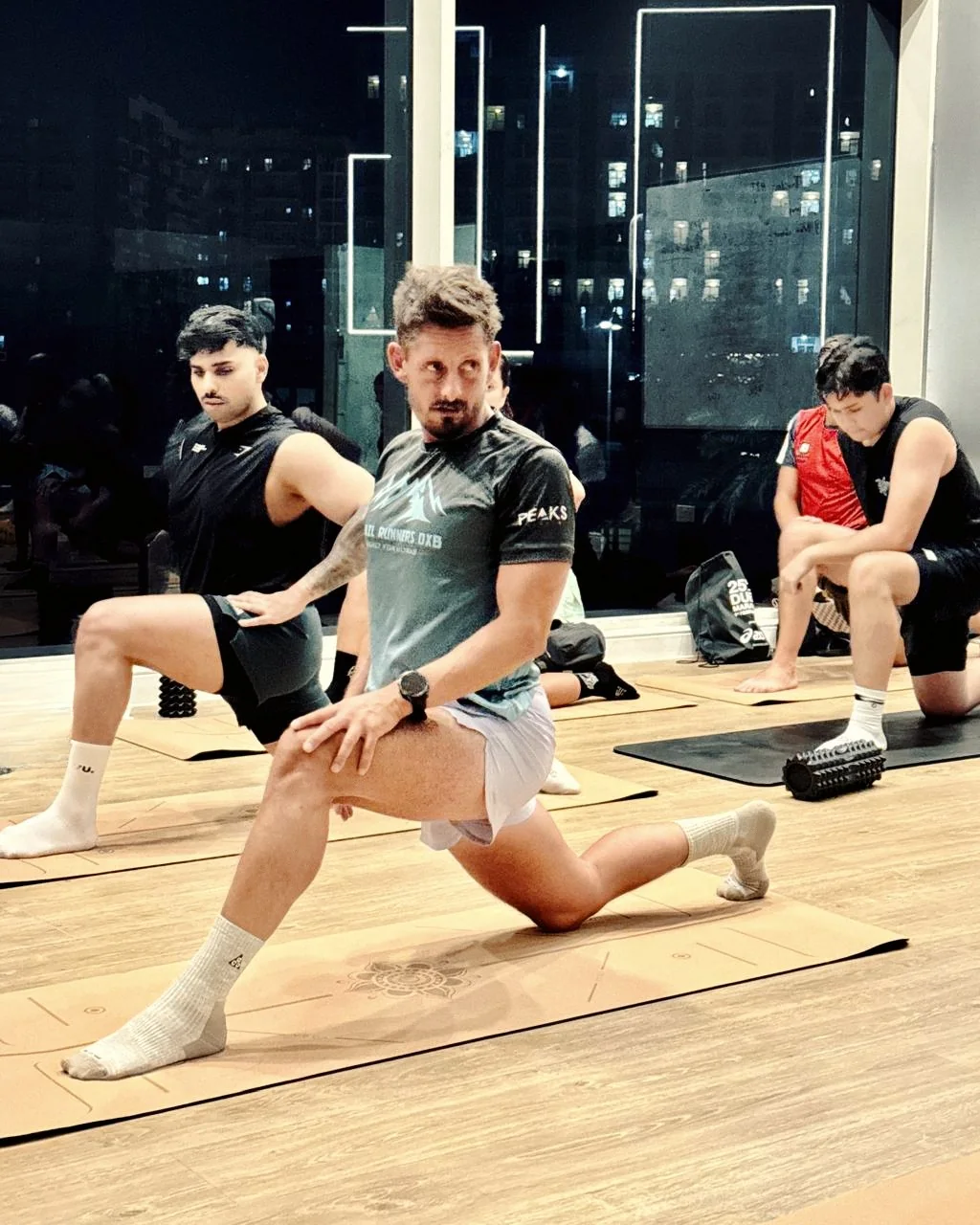 Hybrid athletes holding a deep lunge on cork mats in the Zone Zero room, the city lit up behind them