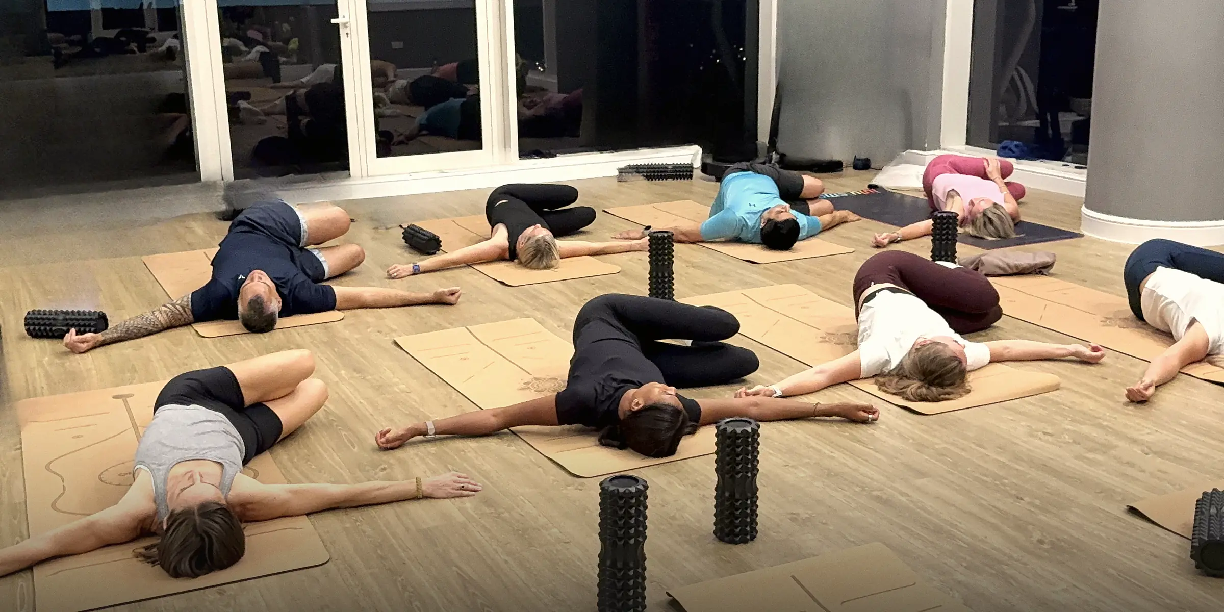 The pilot room near the end of a session: athletes lying on cork mats in a supine twist, rollers standing beside them